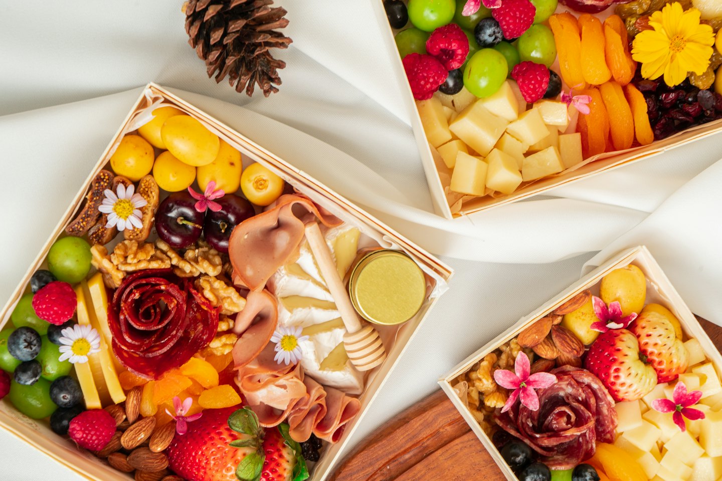 Three charcuterie boxes filled with cheese, fruit, and meat.