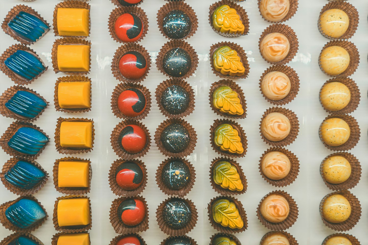 Assorted artisanal chocolates arranged in neat rows on white.